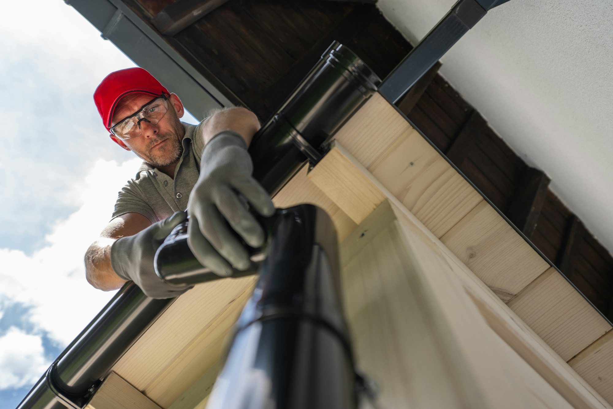 Man Cleaning Gutters on a Residential Roof on a Sunny Day